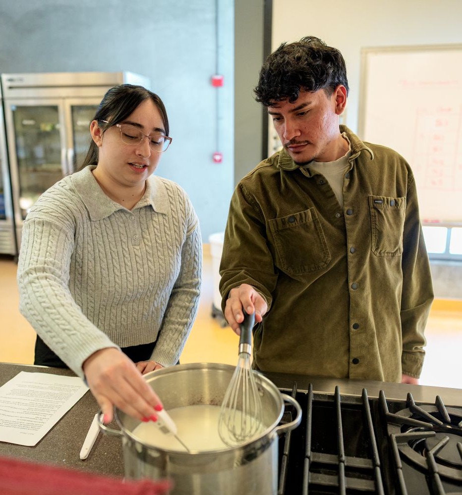 Two young adults stirring a saucepan together on a stove in a kitchen