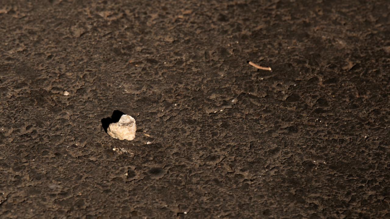 Small white rock in the shape of a heart on black asphalt 