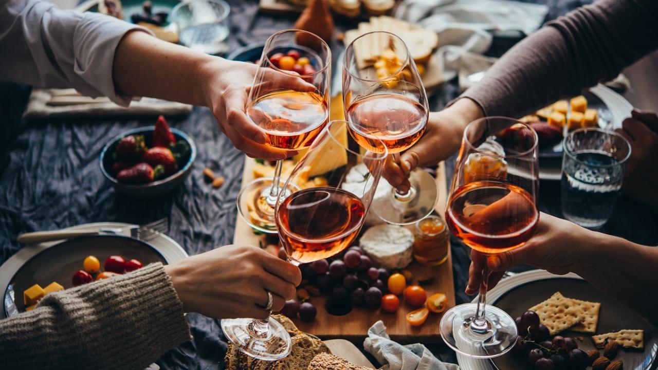 Four hands holding glasses of wine, toasting over a table full of food