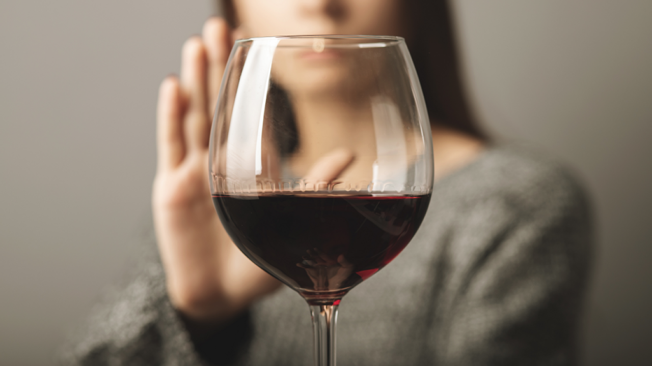 Glass of wine with a person behind it with a hand up to say "no"