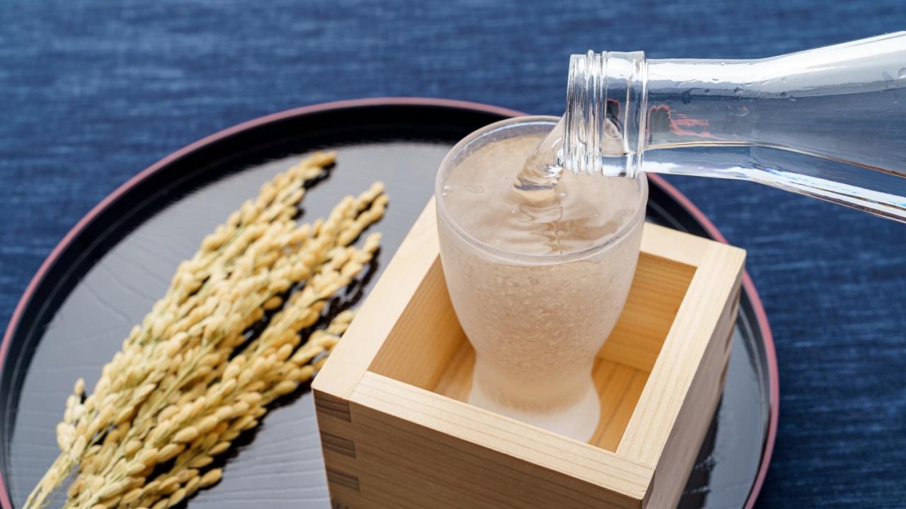 Sake pouring into a glass inside a wooden box with rice on the side