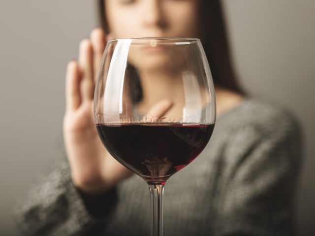Glass of wine with a person behind it with a hand up to say "no"