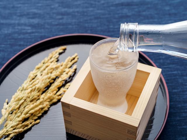 Sake pouring into a glass inside a wooden box with rice on the side