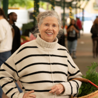 Smiling Ann Evans woman in black-and-white striped sweater at outdoor farmers' market, photograph by Gregory Urquiaga, UC Davis