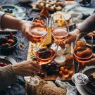Four hands holding glasses of wine, toasting over a table full of food