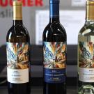 Three wine bottles, two red and one white, with colorful abstract labels on a counter