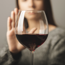 Glass of wine with a person behind it with a hand up to say "no"
